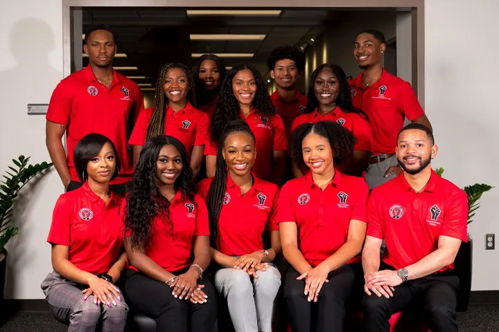Twelve students in matching red polos with raised-fist logos posed in two rows for an officer group portrait