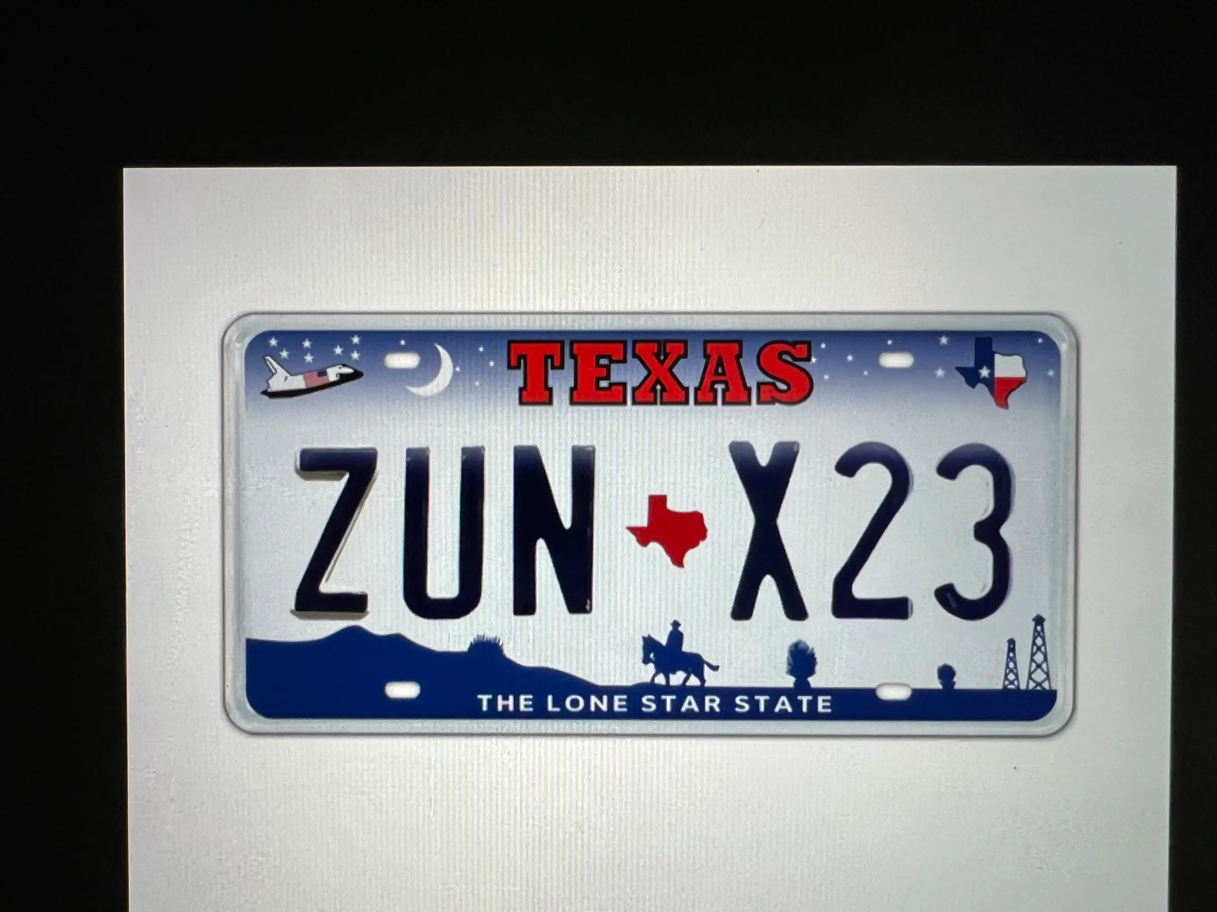 Texas license plate mockup reading ZUN X23 with space shuttle, cowboy and oil derrick graphics, shown on a screen