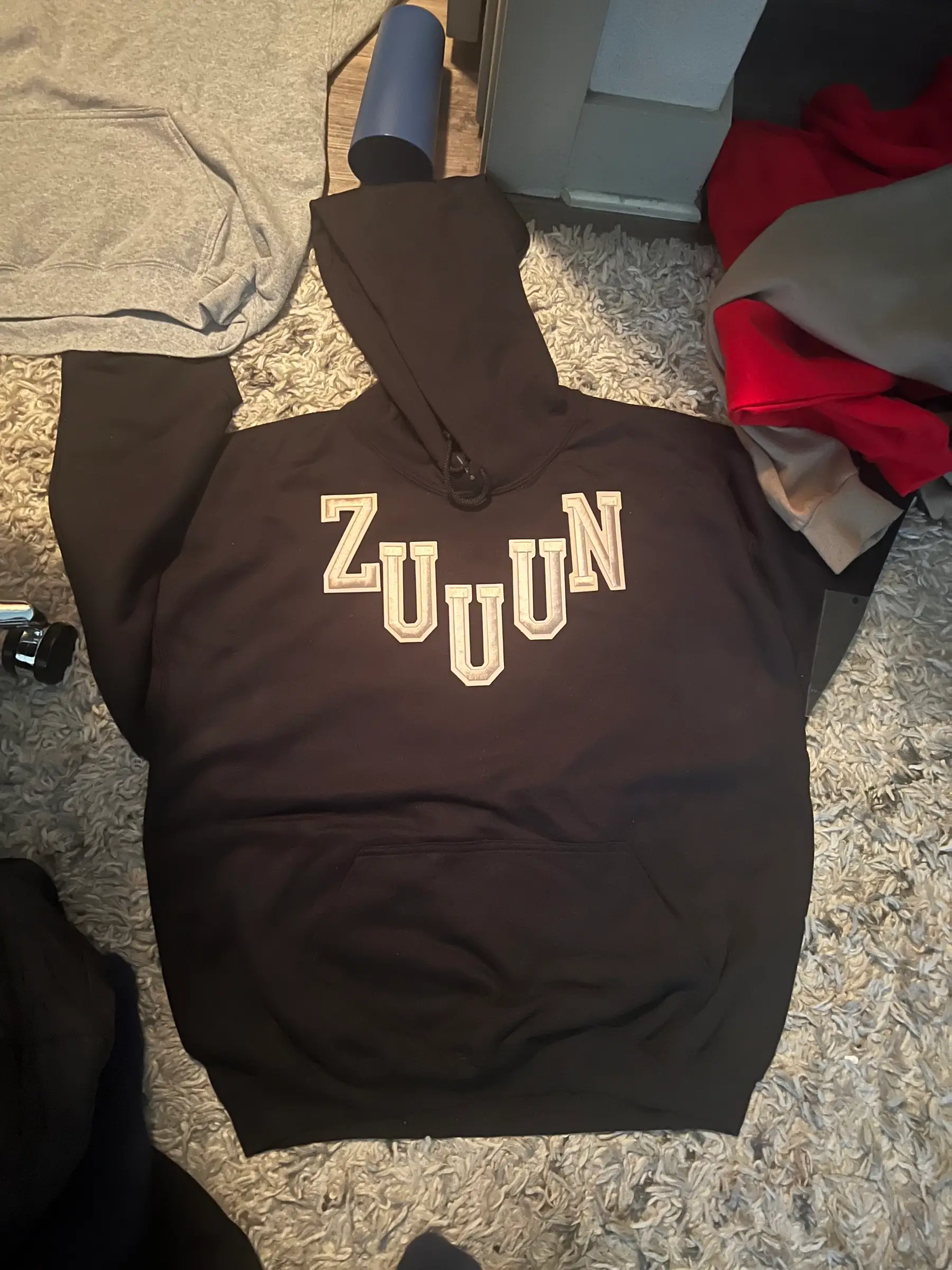 Black hoodie on a shag rug with Z-U-U-U-N patch letters arranged in a dipping curve